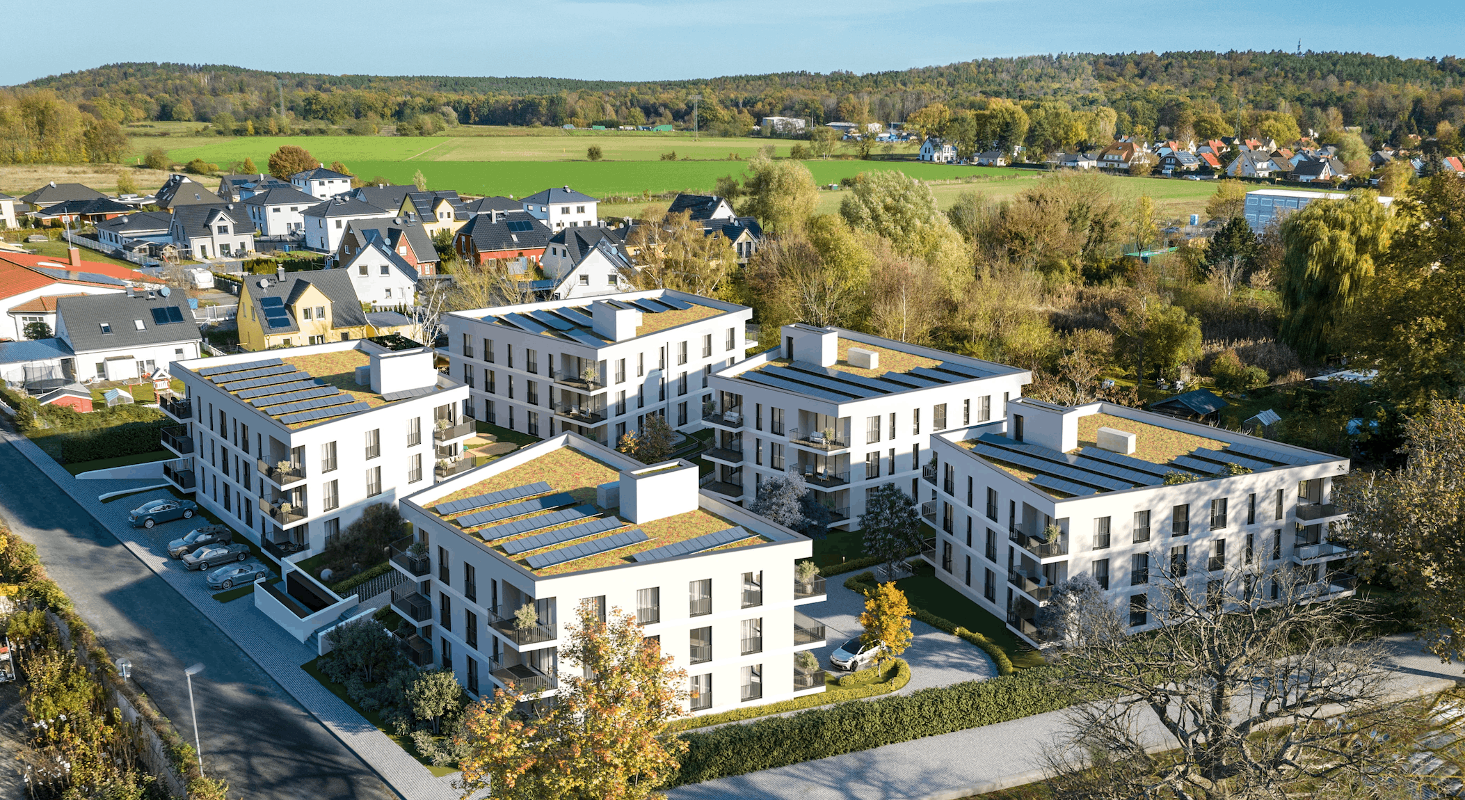 Fotorealistische 3D-Architekturvisualisierung eines modernen Neubauquartiers aus der Vogelperspektive. Die detaillierte Luftaufnahme zeigt ein geplantes Wohnprojekt mit mehreren weißen Mehrfamilienhäusern, die mit nachhaltigen Gründächern und Photovoltaikanlagen ausgestattet sind. Moderne Balkone, großzügige Fensterfronten und ansprechende Außenanlagen mit Parkplätzen runden das Architekturkonzept ab. Die Gebäude fügen sich harmonisch in die umliegende grüne Vorstadtlandschaft ein – ein ideales Bild für die professionelle Immobilienvermarktung und Projektentwicklung.